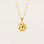 Gold sun-shaped pendant necklace on a light beige background