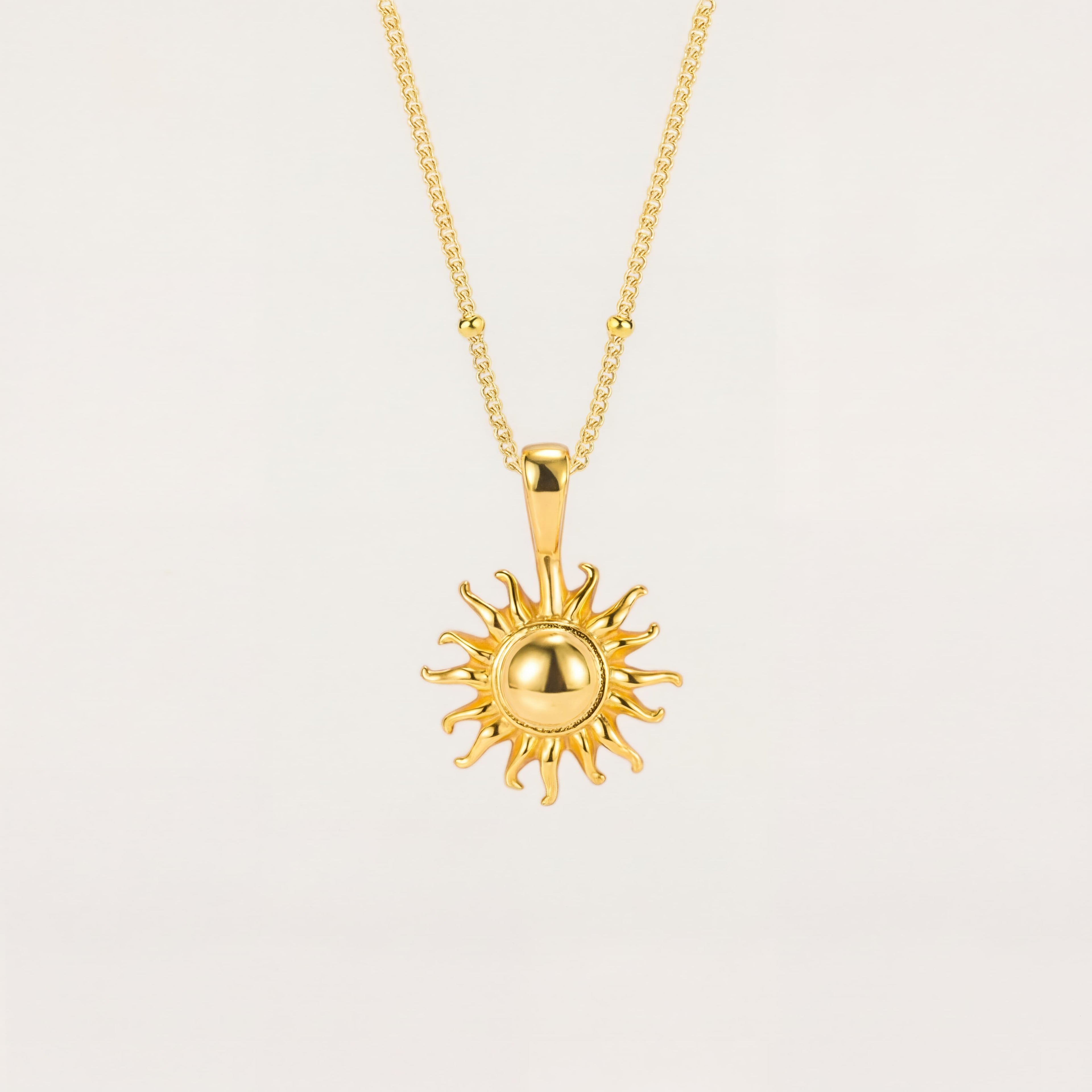 Gold sun-shaped pendant necklace on a light beige background